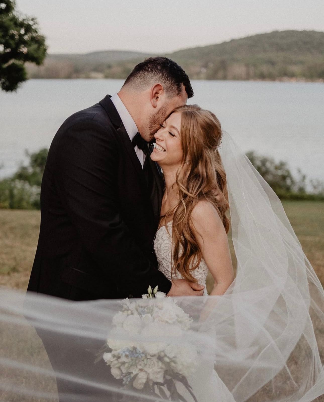 A bride and groom are posing for a picture with their veil blowing in the wind.