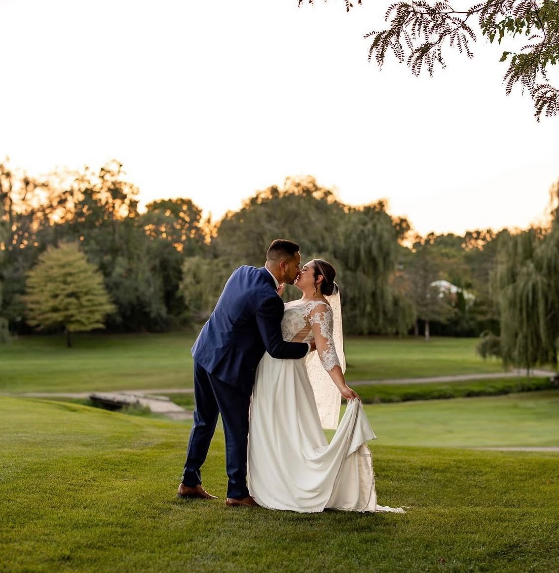 A bride and groom are kissing in the grass on a golf course.