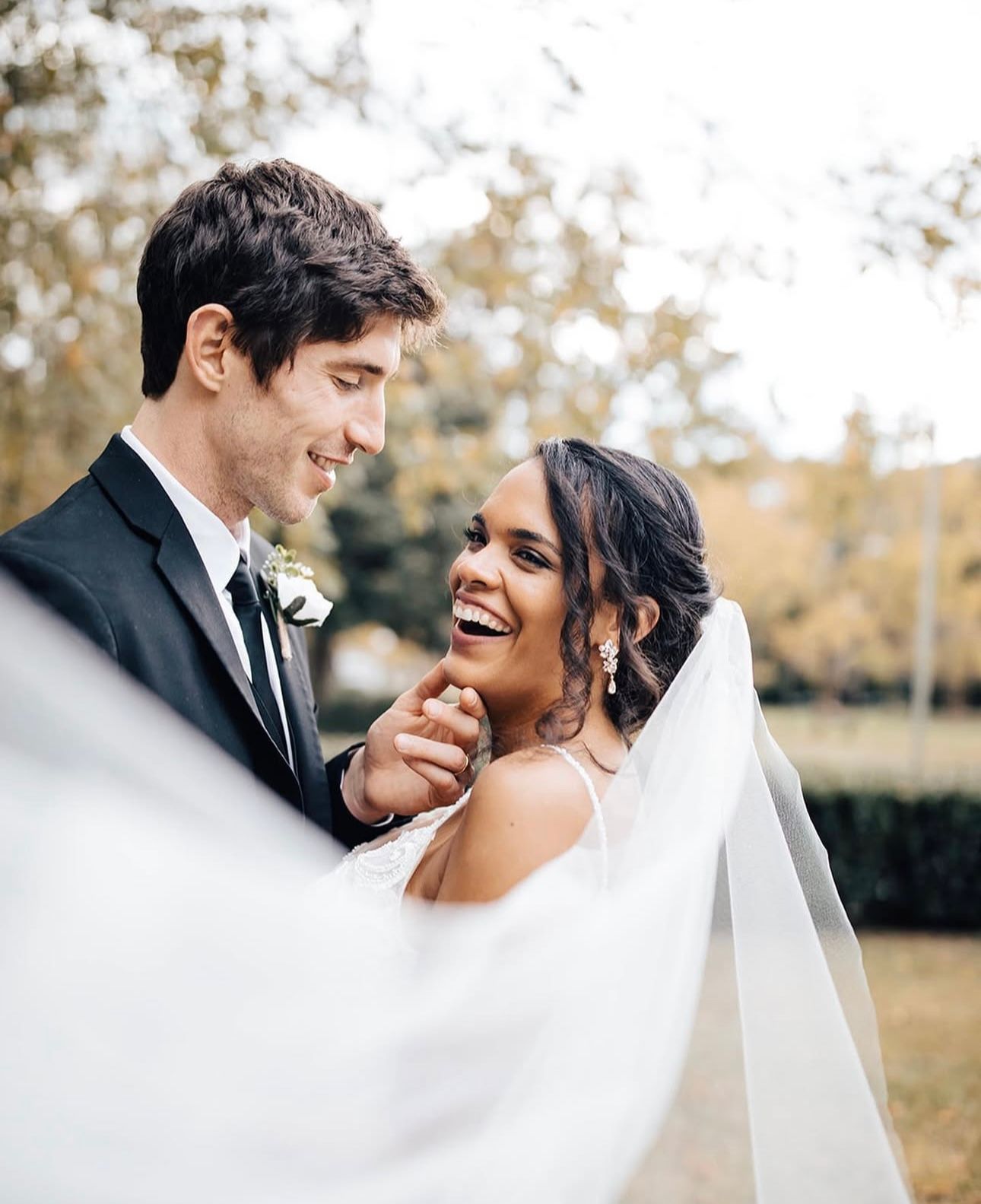 A bride and groom are posing for a picture while the bride 's veil is blowing in the wind.