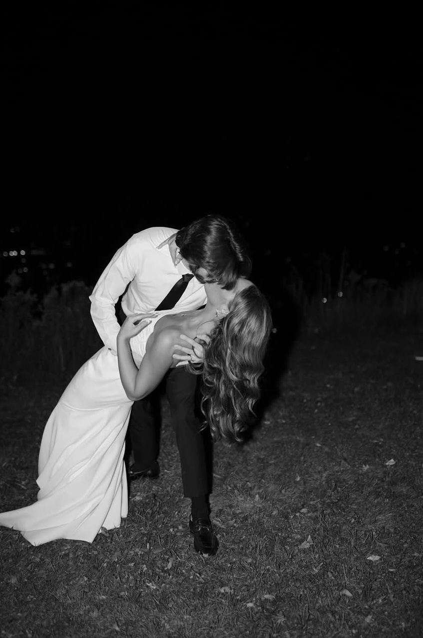 A black and white photo of a bride and groom kissing in the grass.