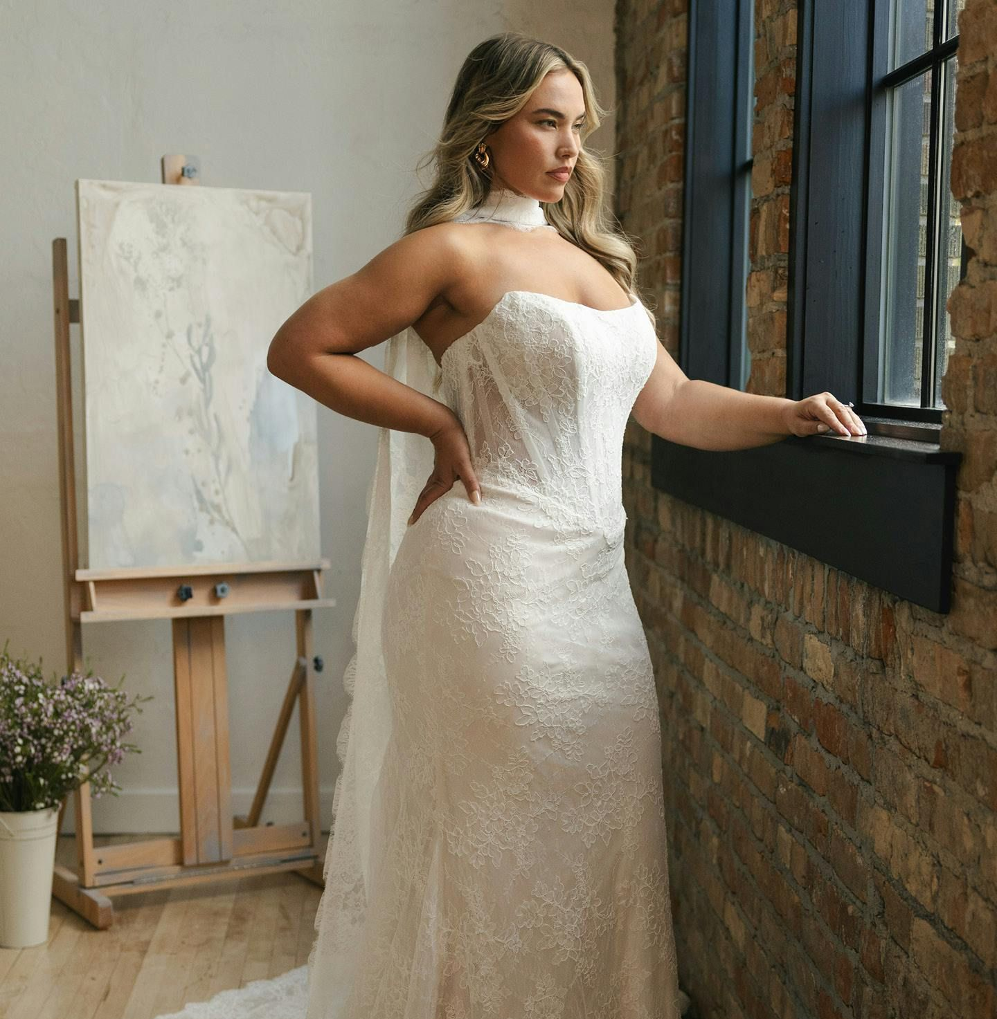 A woman in a white wedding dress is standing in a room surrounded by flowers.