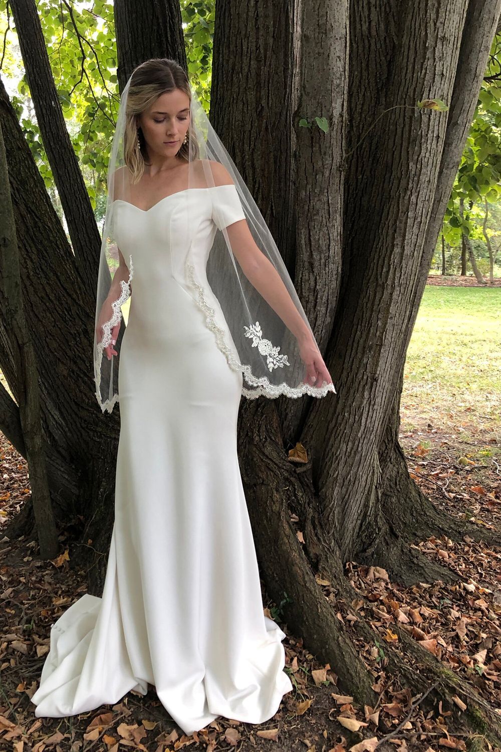 A woman in a wedding dress and veil is standing next to a tree.
