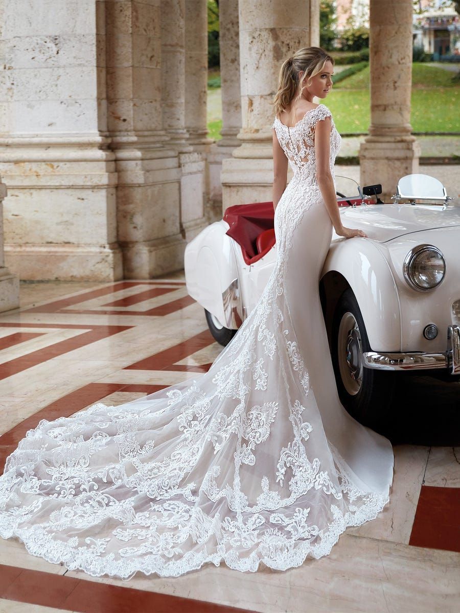 A woman in a wedding dress is leaning against a white car.