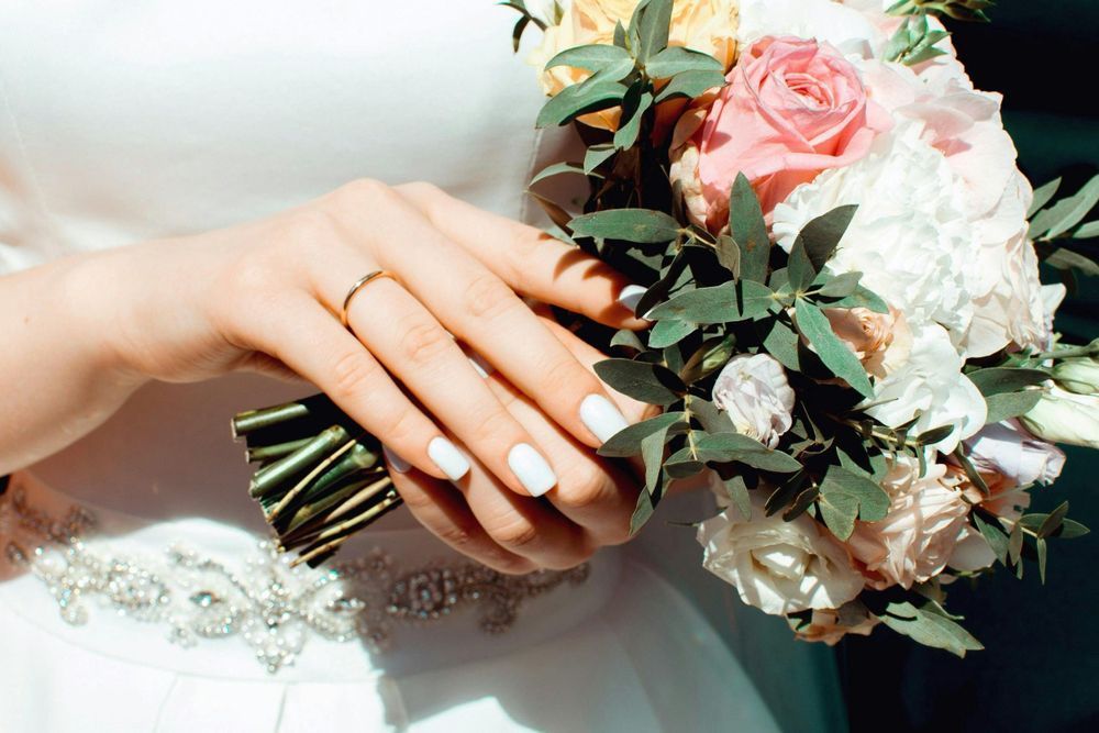 The bride is wearing a wedding ring and holding a bouquet of flowers.
