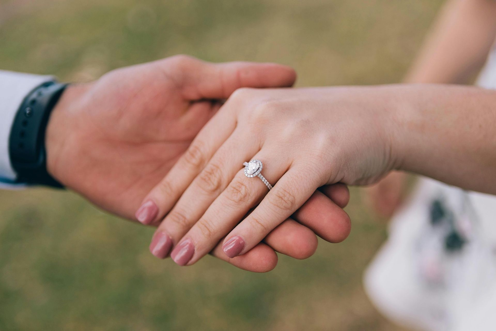 A man and a woman are holding hands and the woman has an engagement ring on her finger.