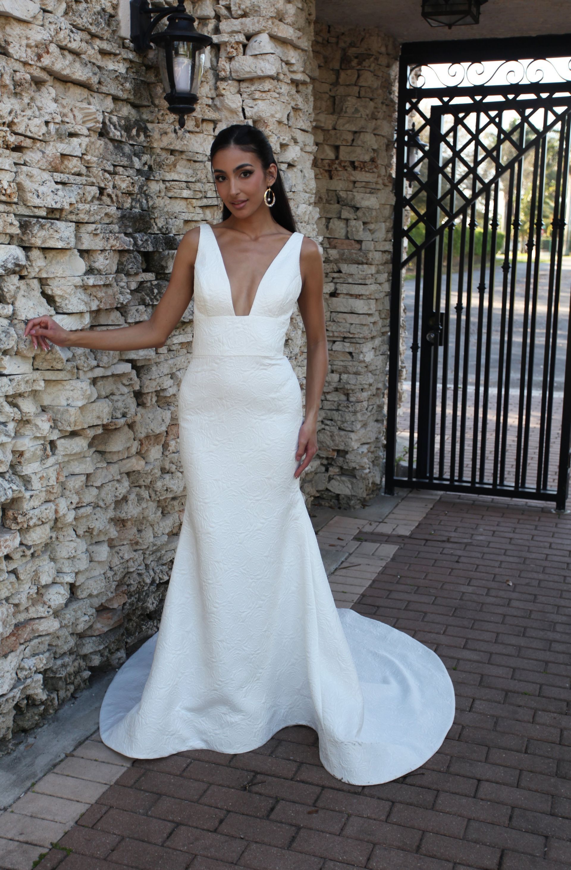 A woman in a white wedding dress is standing in front of a stone wall.