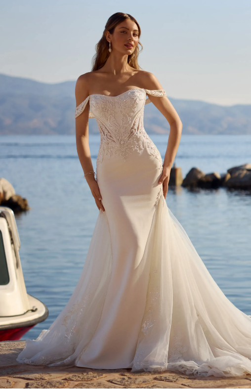 A woman in a wedding dress is standing in front of a body of water.