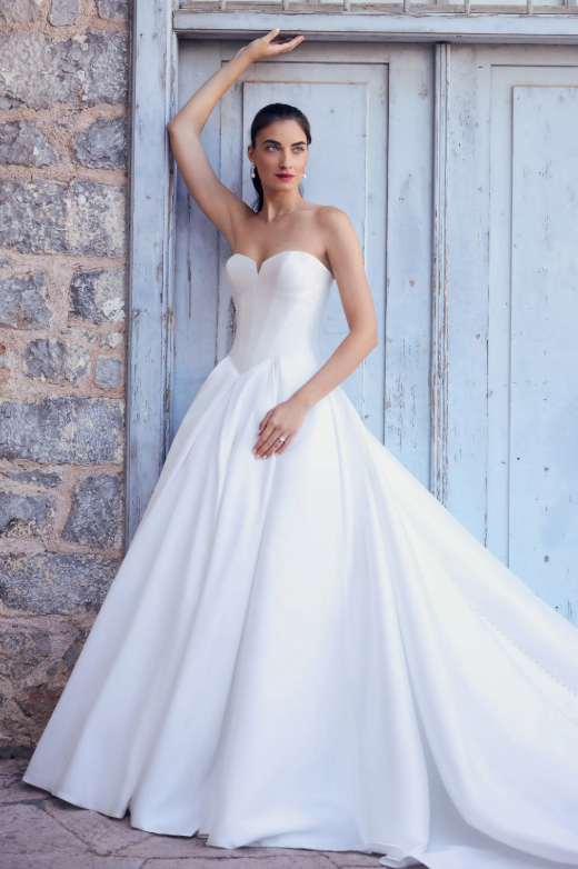 A woman in a white wedding dress is leaning against a blue door
