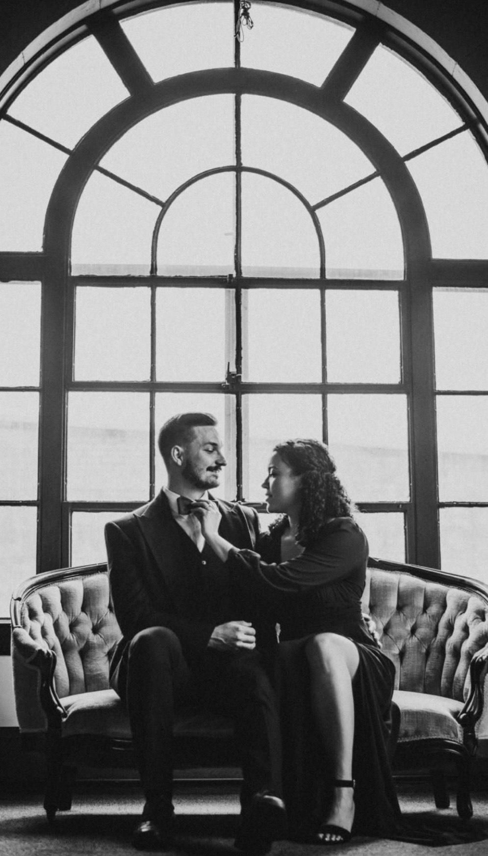 A man and a woman are sitting on a couch in front of a window.