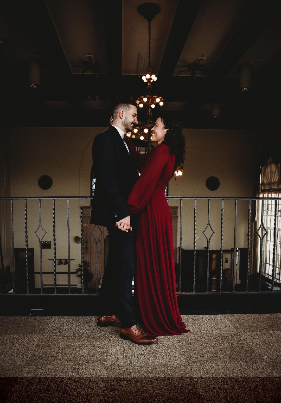 A man and a woman are holding hands in a dark room . the woman is wearing a red dress.