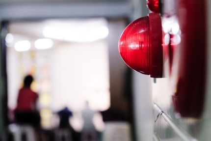 Blue-toned view of an industrial light fixture with people blurred in the background, possibly indoors.