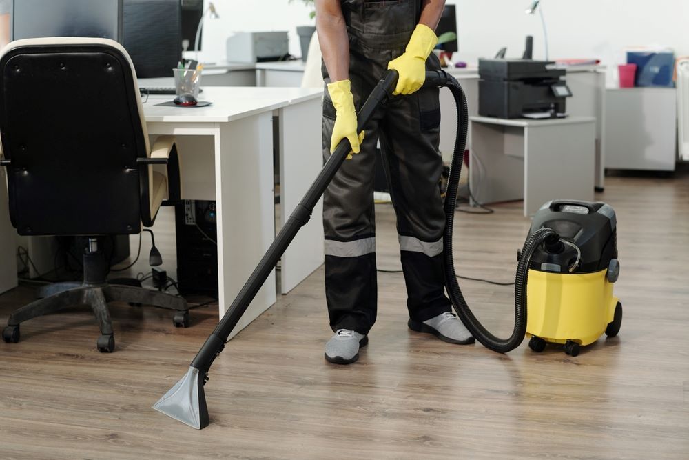 A Man is Cleaning the Floor of an Office With a Vacuum Cleaner — O & D House Wash & Cleaning Services in Westbrook, QLD