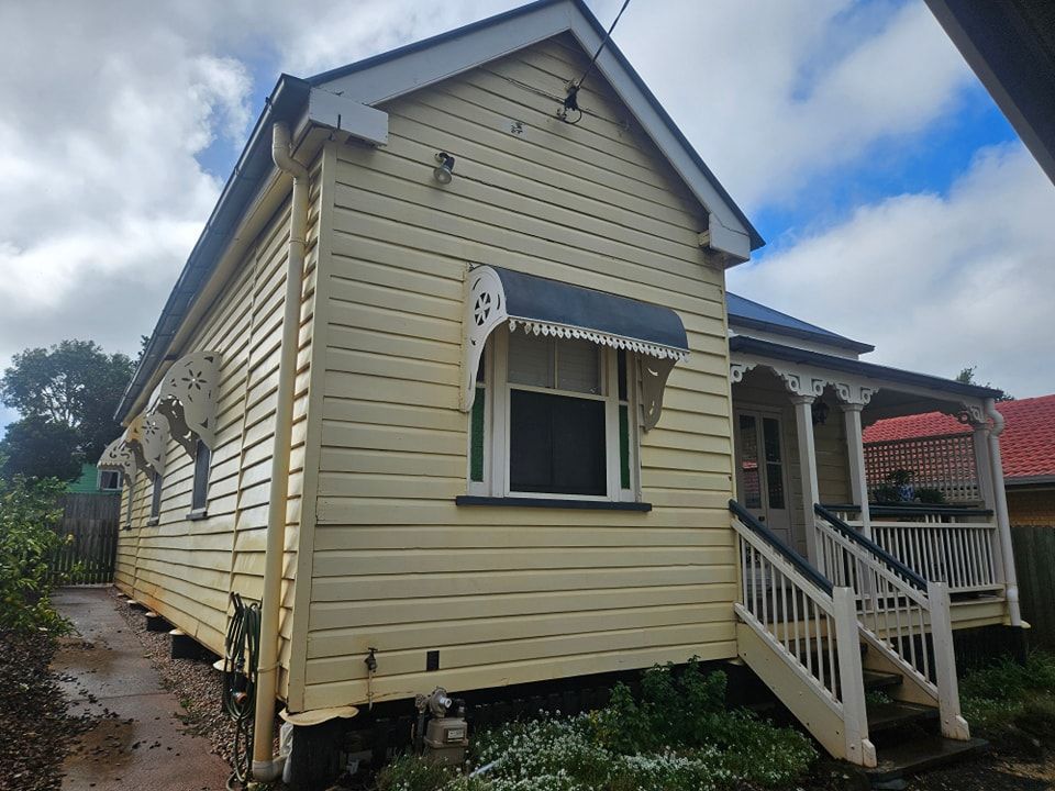 A Small Yellow House With a Porch and Stairs — O & D House Wash & Cleaning Services in Cambooya, QLD