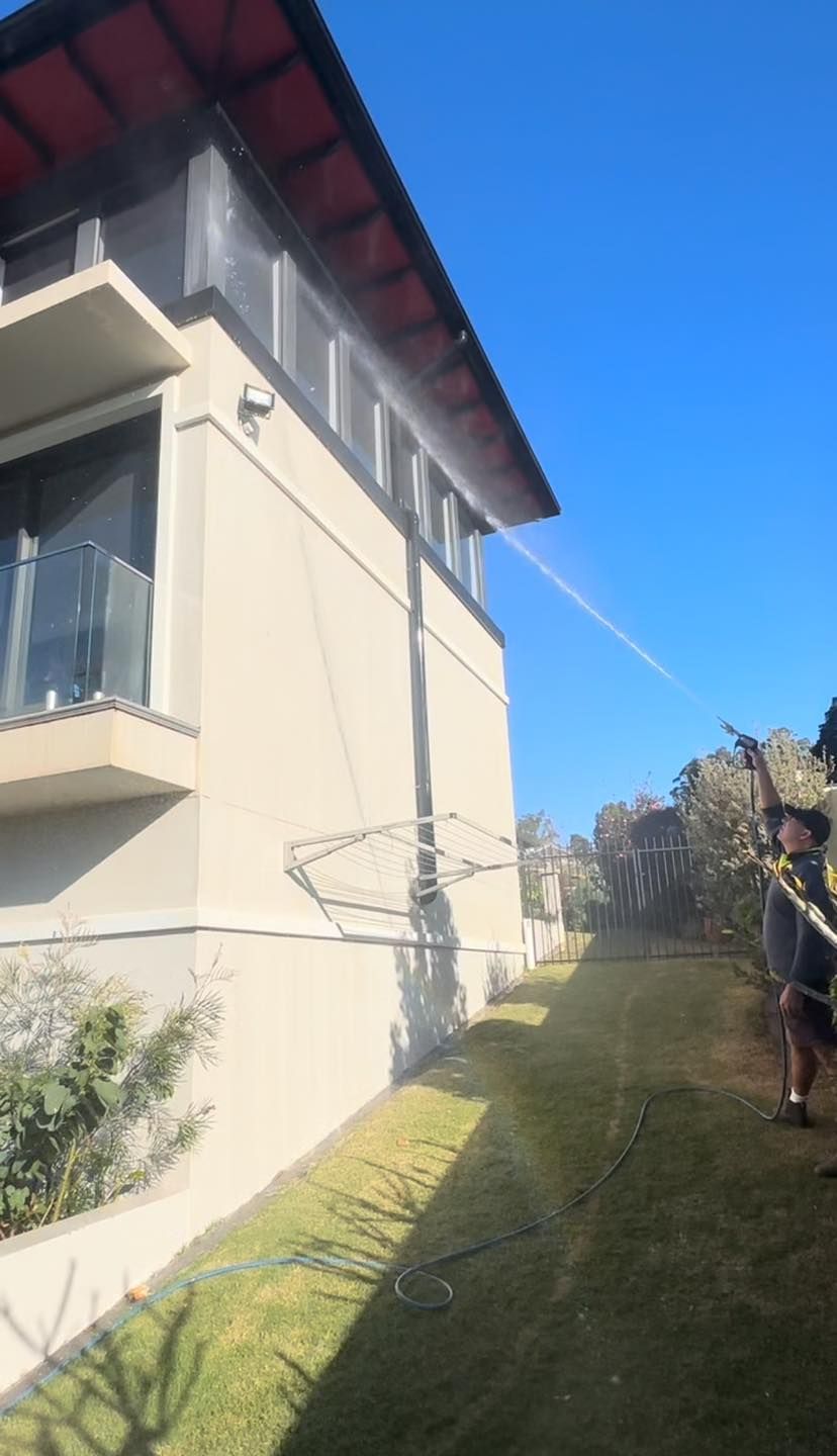 A Man is Spraying Water on the Side of a Building — O & D House Wash & Cleaning Services in Cambooya, QLD
