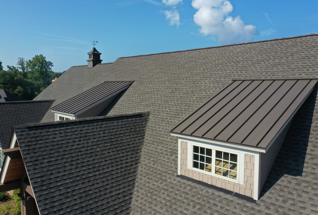Aerial view of a gray shingled roof with dormer windows under a blue sky