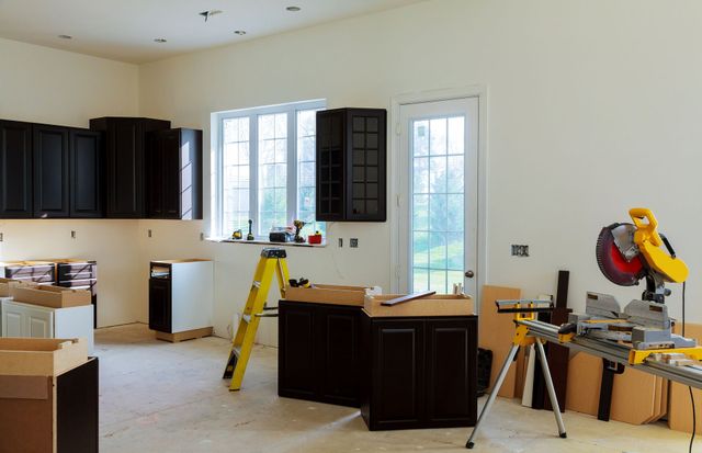 Kitchen under renovation with dark cabinets, tools, boxes, and a miter saw on the right