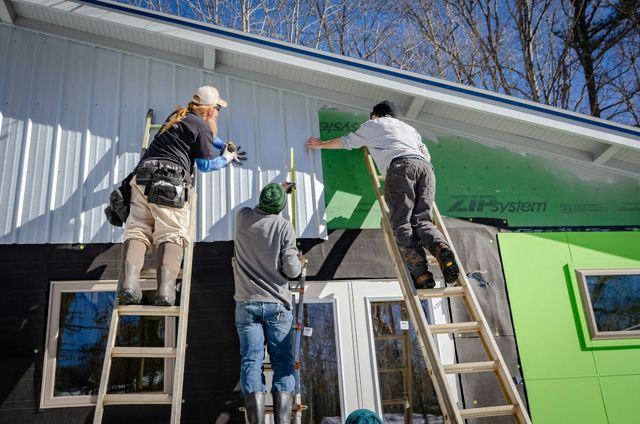 Three workers on ladders painting the exterior wall of a green and white building