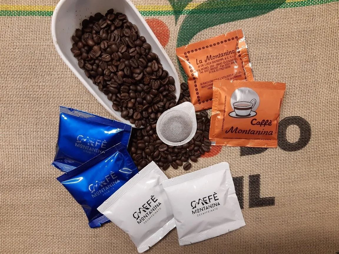 Una manciata di chicchi di caffè tostati scuri e diverse bustine campione di caffè sparse su una superficie ruvida e decorata.