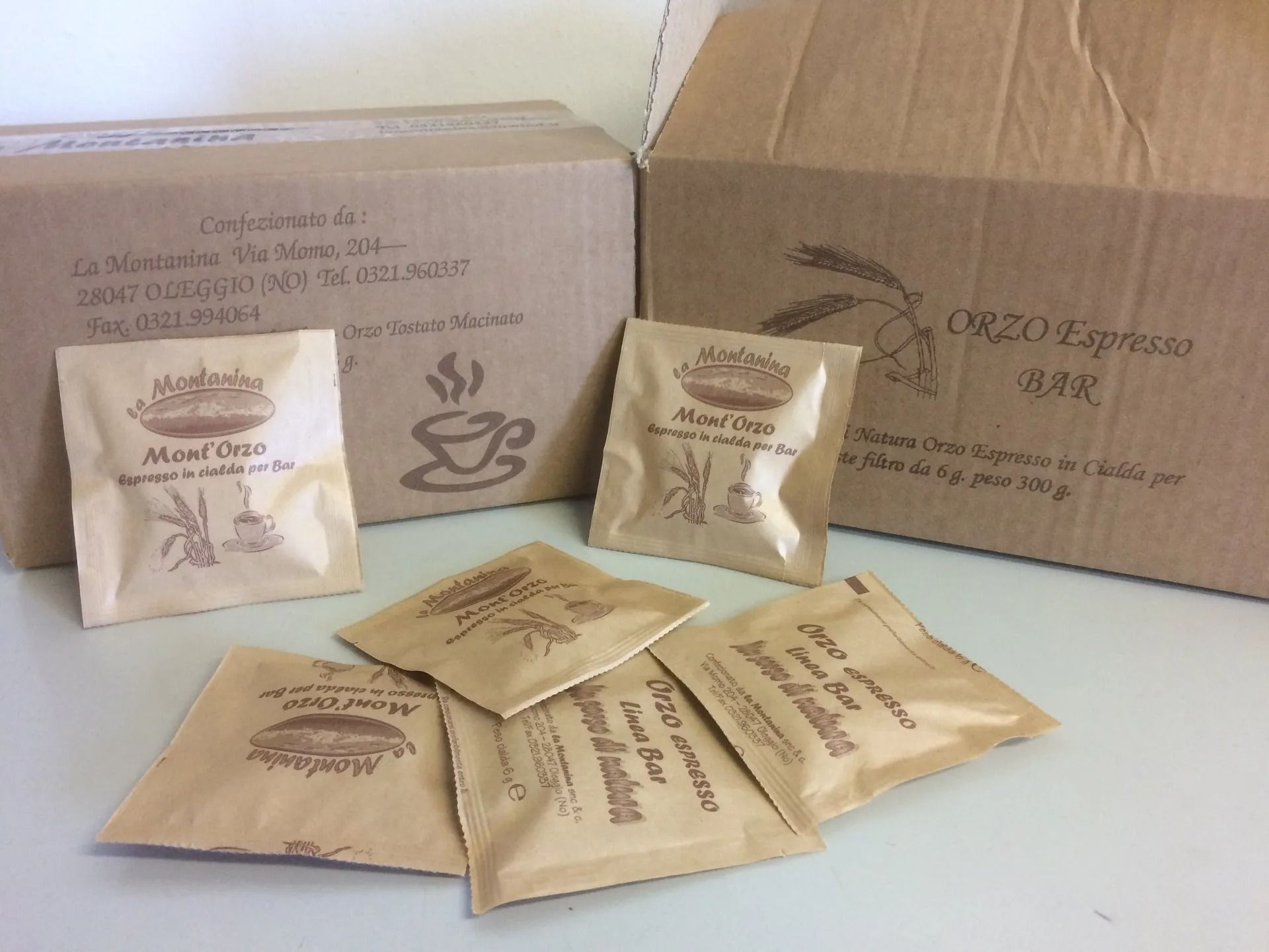 Diverse piccole bustine di carta di caffè espresso Orto sono sparse davanti a due scatole di cartone con il logo del marchio.