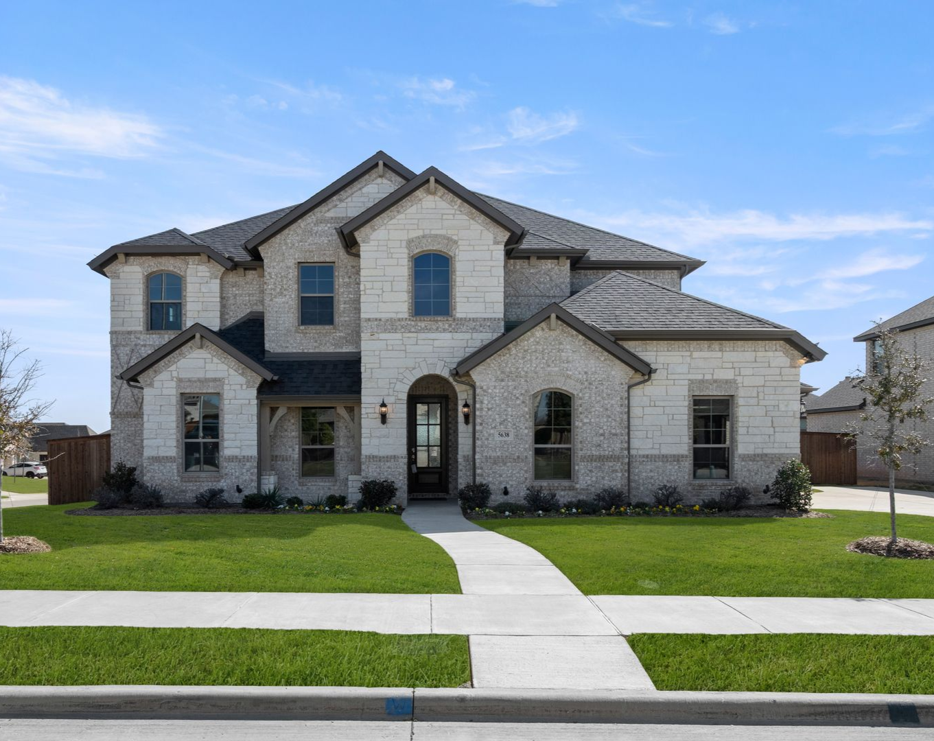 Brick and wood-sided house with a large green lawn under a partly cloudy sky.