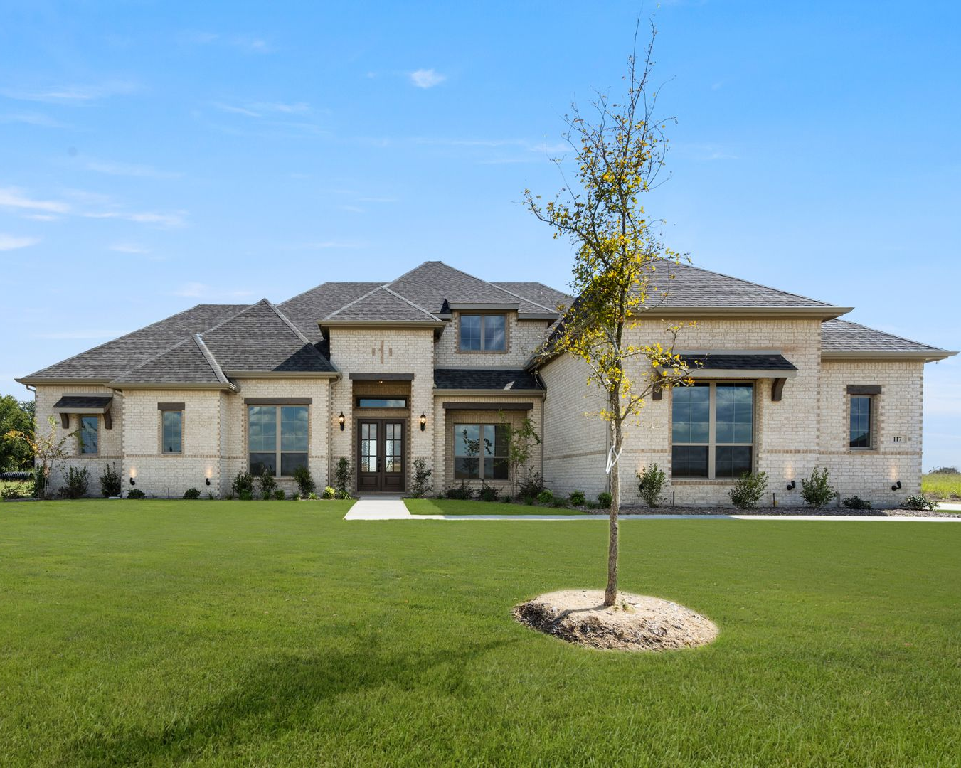Stone-fronted house with a dark roof and manicured lawn under a blue sky.