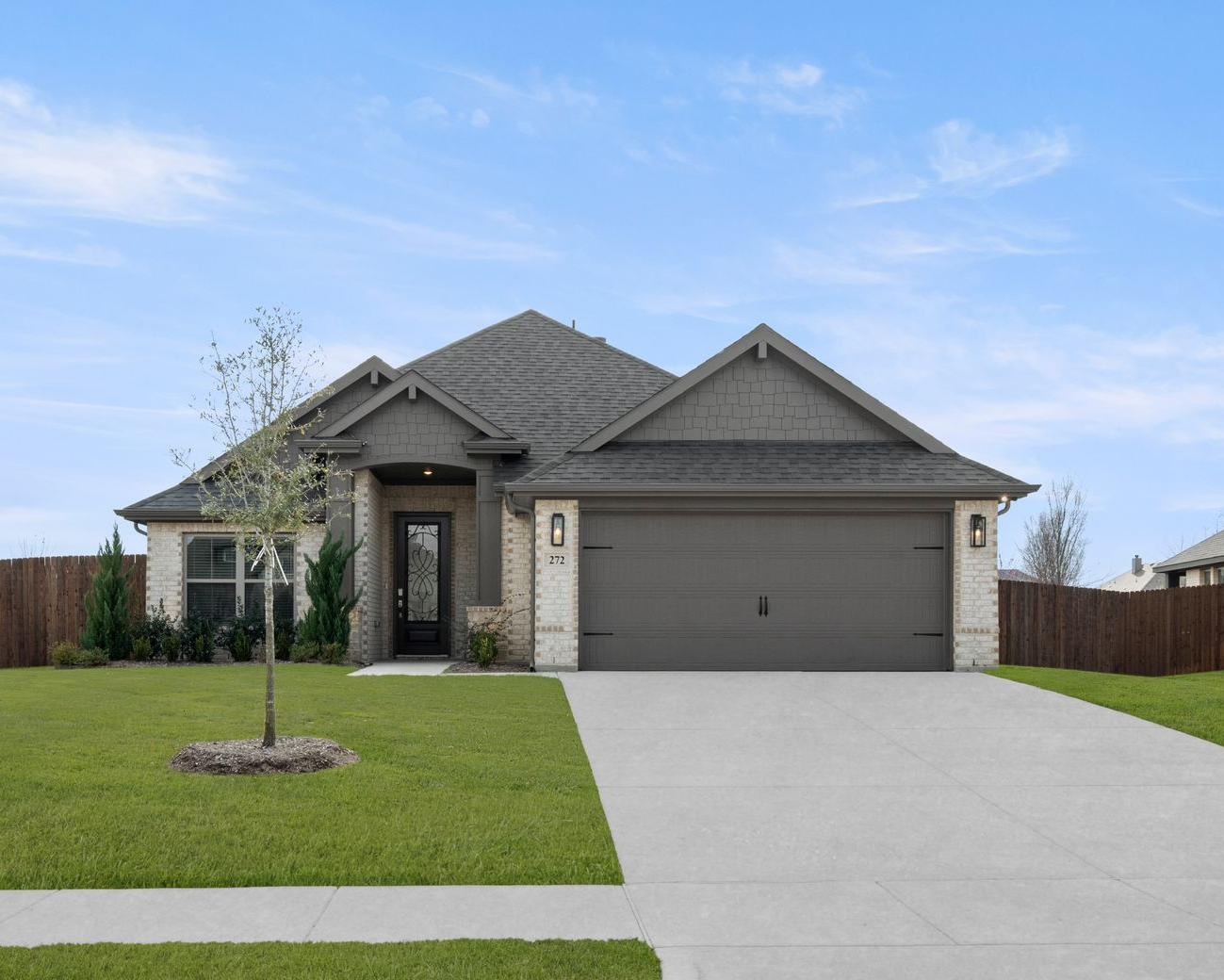 Two-story brick house with stone accents, gray roof, garage door, green lawn, and blue sky.