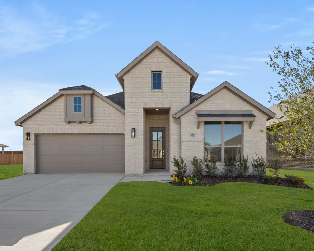 Stone-fronted house with a dark roof and manicured lawn under a blue sky.