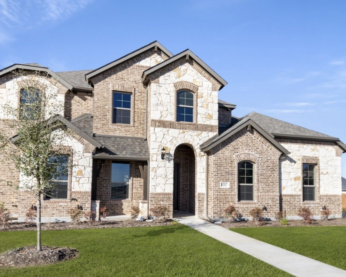 Stone-fronted house with a dark roof and manicured lawn under a blue sky.