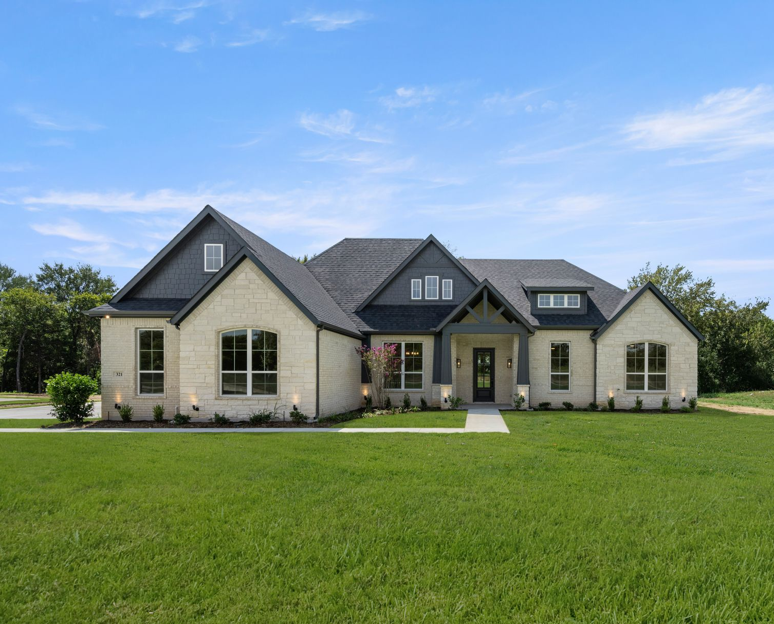 A two-story house with a tan garage door, brick and stone exterior, and green lawn.