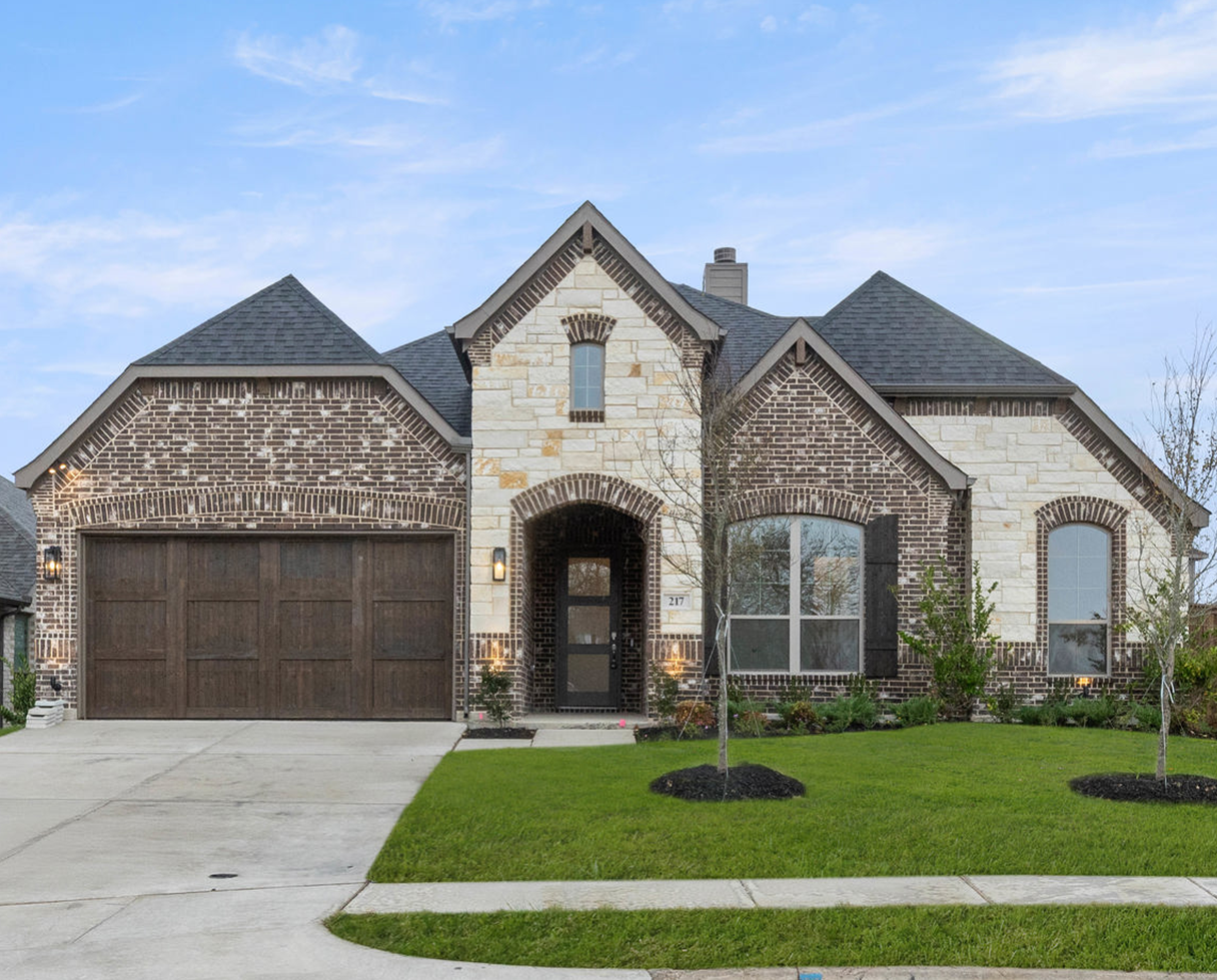Brick house with multiple gables on a grassy lot under a blue sky.