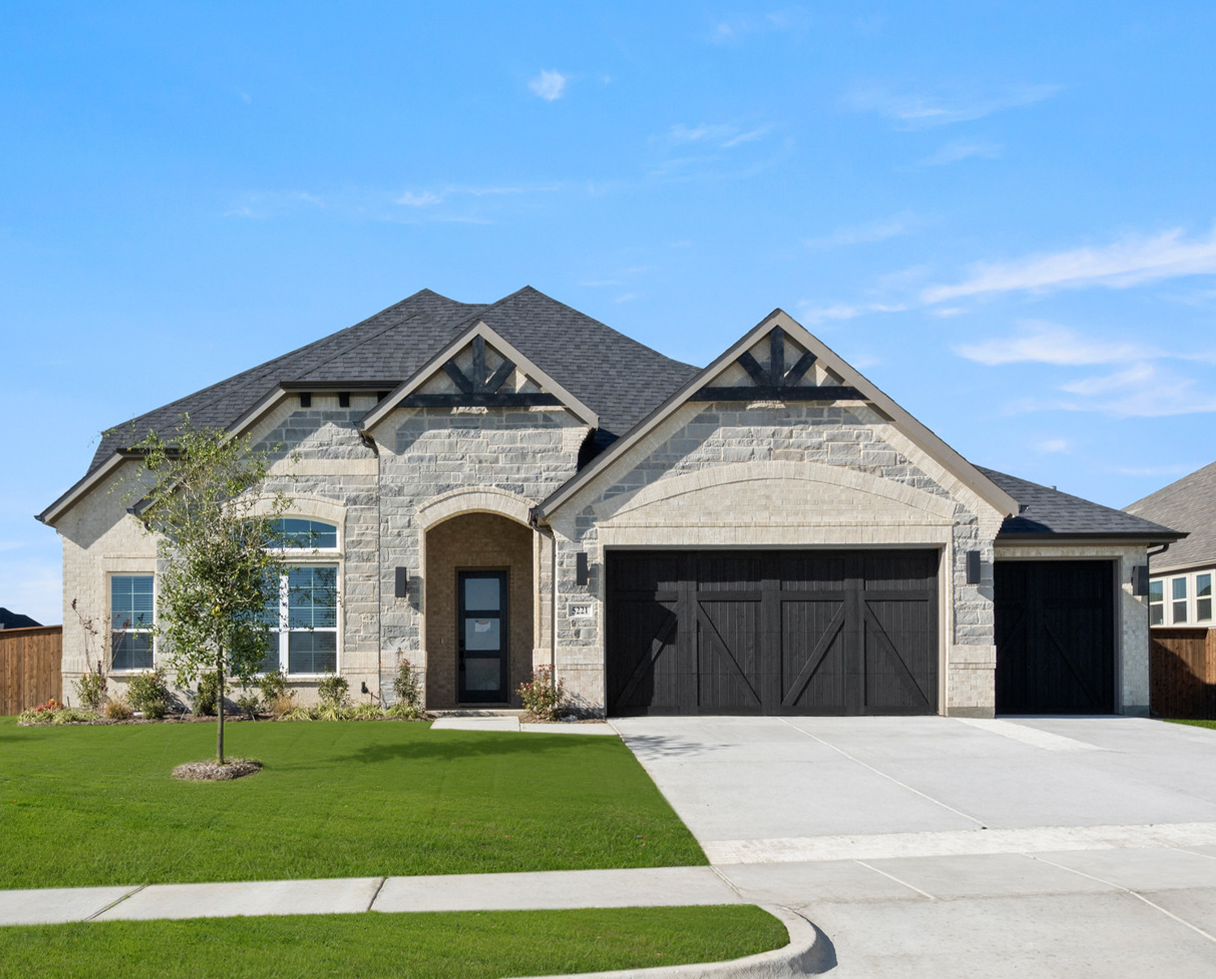 Brick house with multiple gables on a grassy lot under a blue sky.