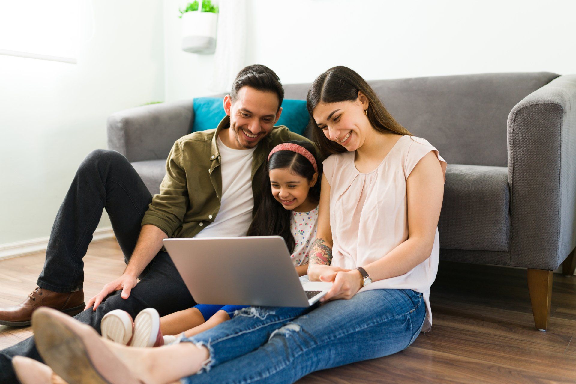A  happy father, mother, and daughter sitting on the floor, looking at a laptop