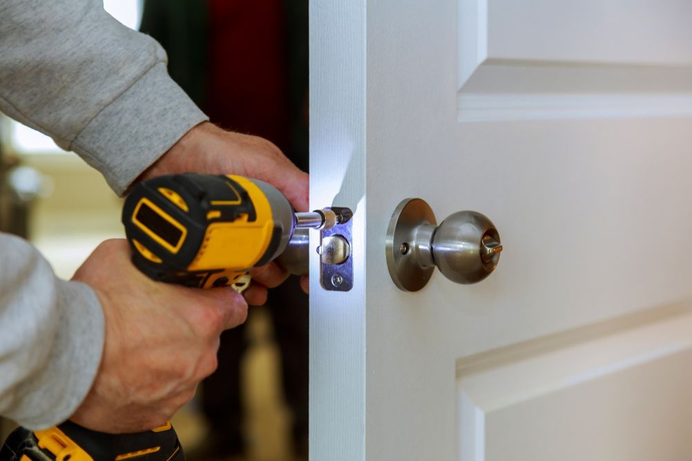A Man Is Fixing A Door With A Drill — Dependable Locksmiths in Wingham, NSW
