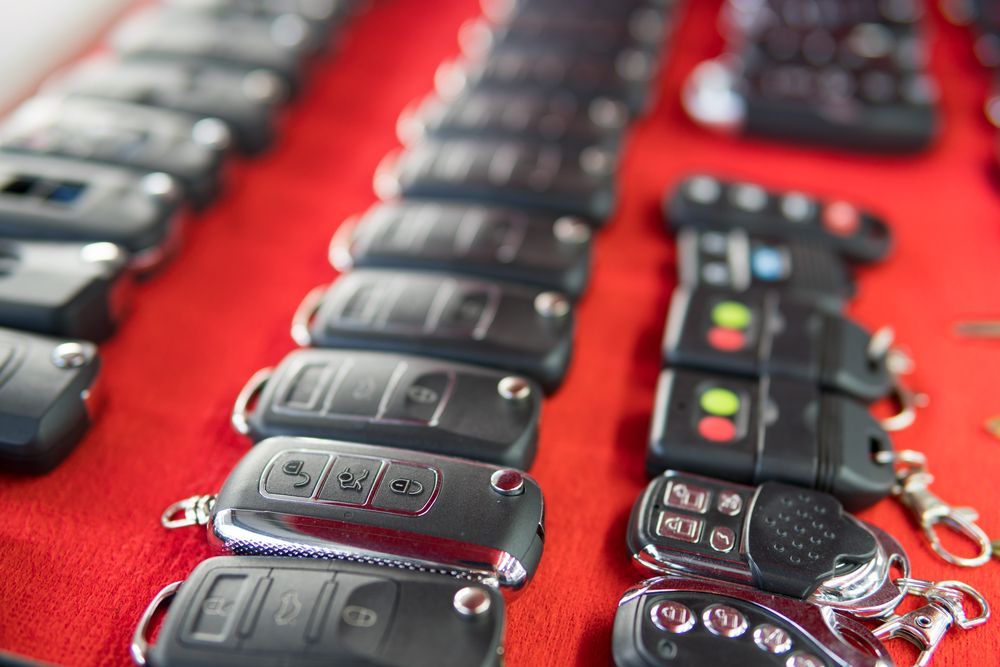Rows of Black Car Key Fobs with Different Button Configurations Displayed on A Red Surface — Dependable Locksmiths In Gloucester, NSW