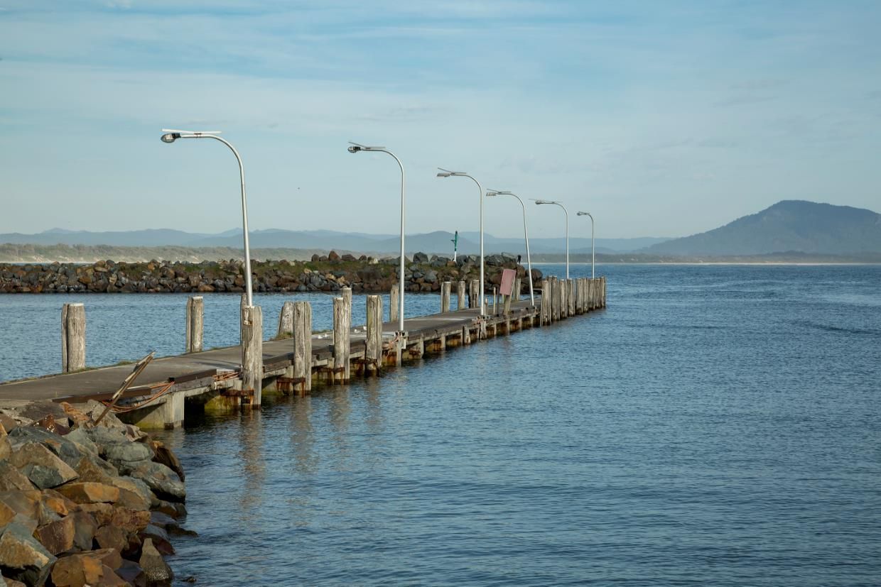 A Dock Leading Into A Body Of Water With Mountains — Dependable Locksmiths In Taree, NSW
