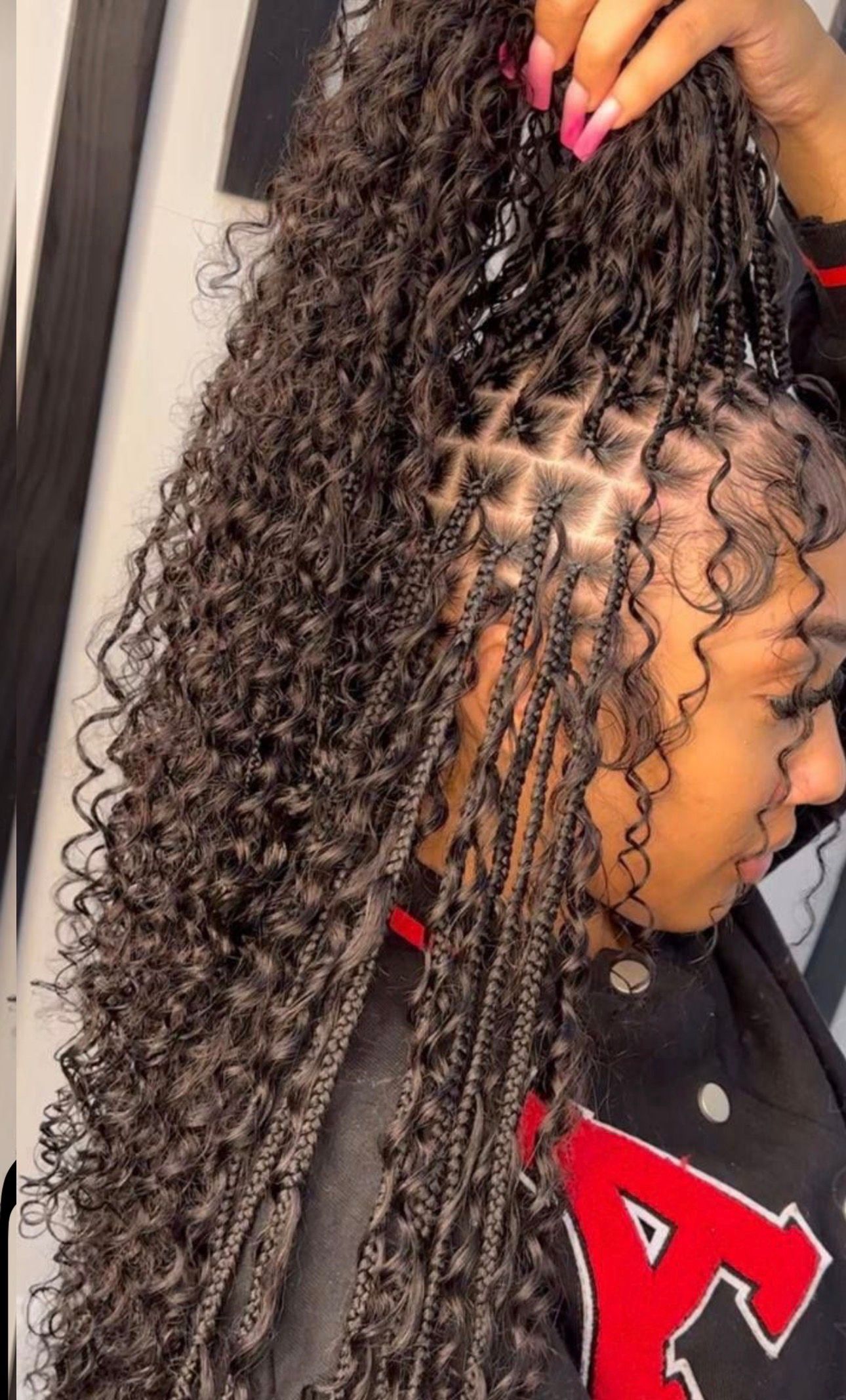 Person having braids styled in a salon. Stylist holding braids; mirror in background.