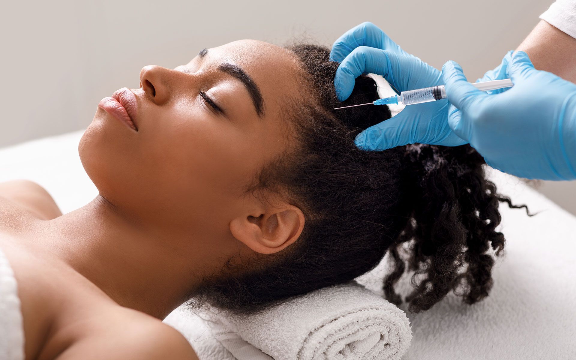 Person receiving a scalp injection; a gloved hand holds a syringe.