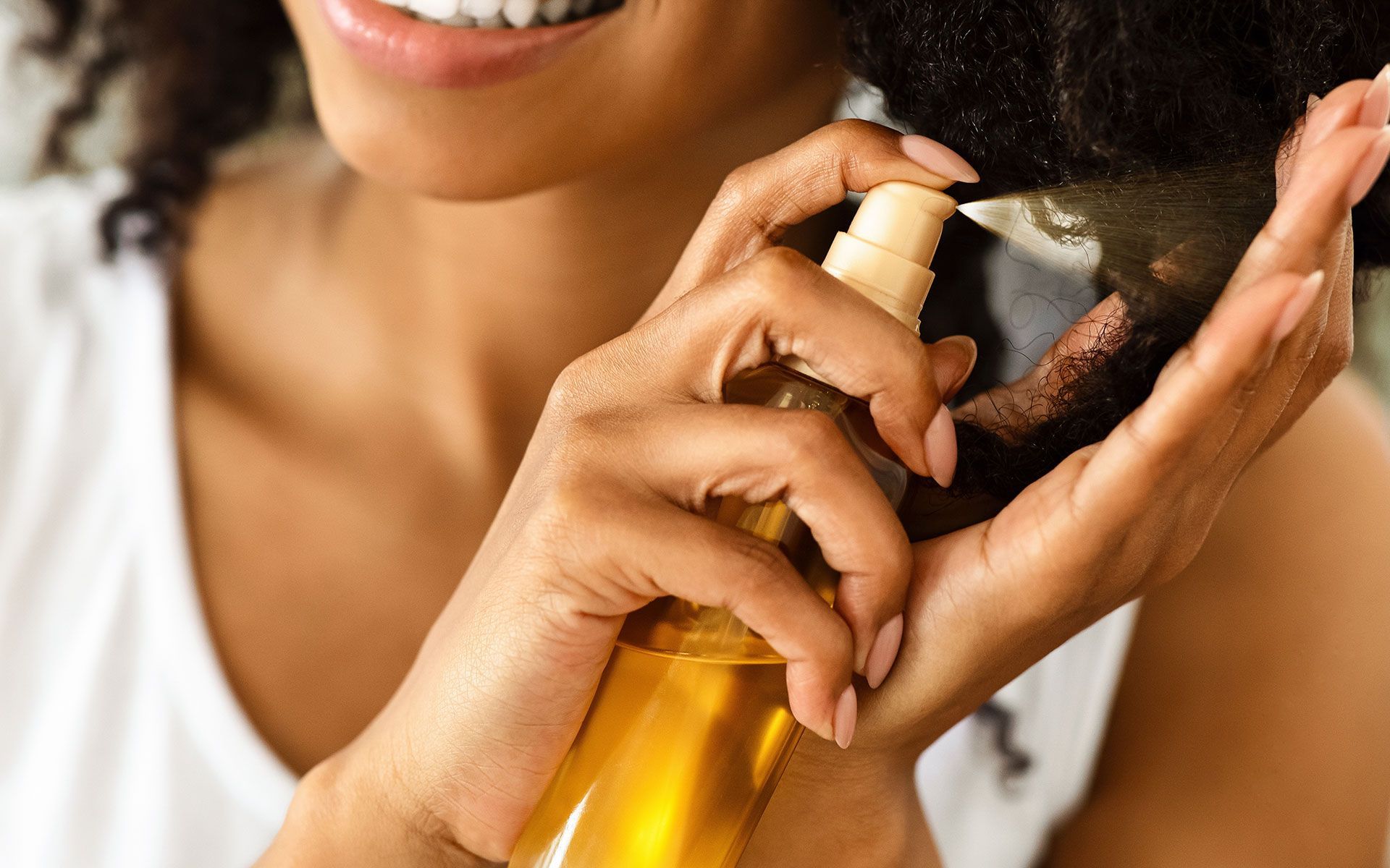 Person spraying hair with a golden liquid from a spray bottle.