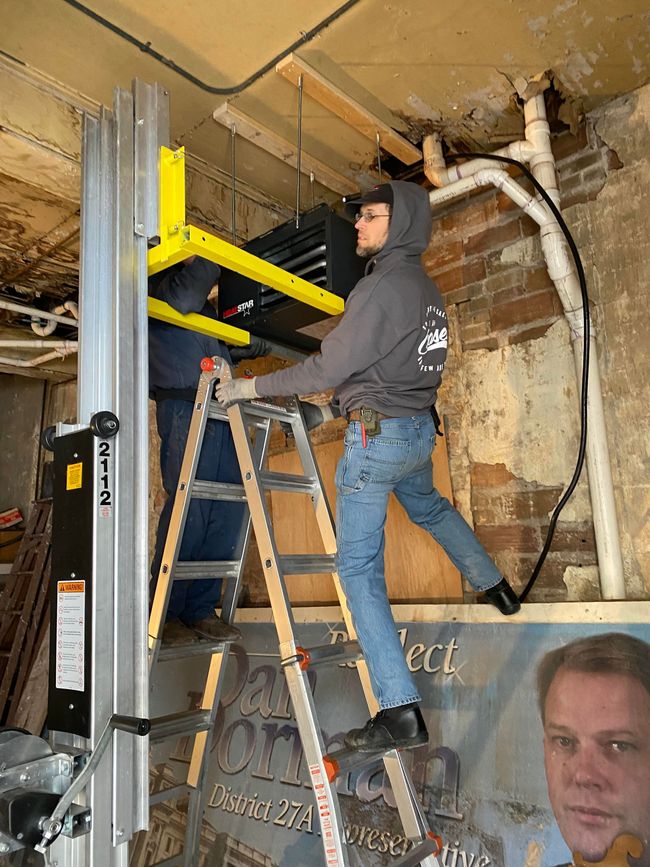 Plumber kneeling beside a bathroom sink, inspecting a faucet with tools on his belt.