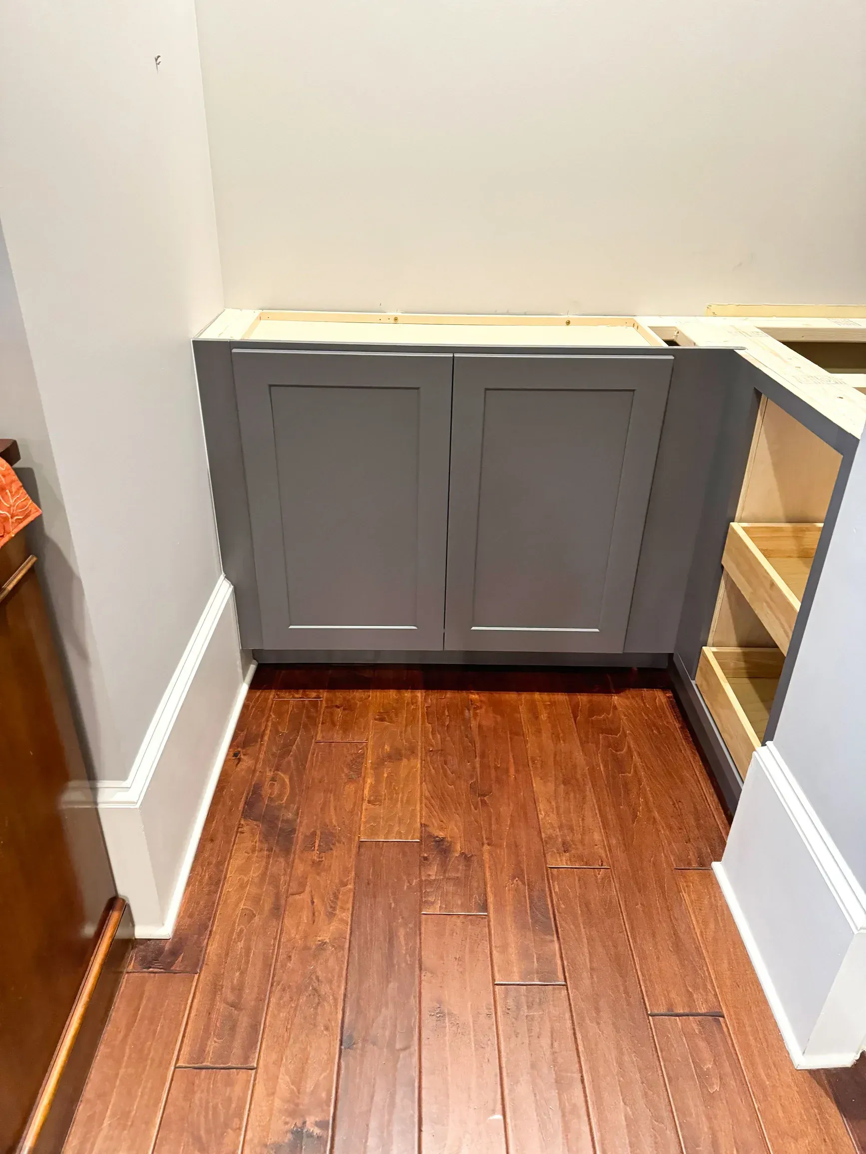 Gray kitchen cabinet with two doors, installed against white walls and hardwood floor.