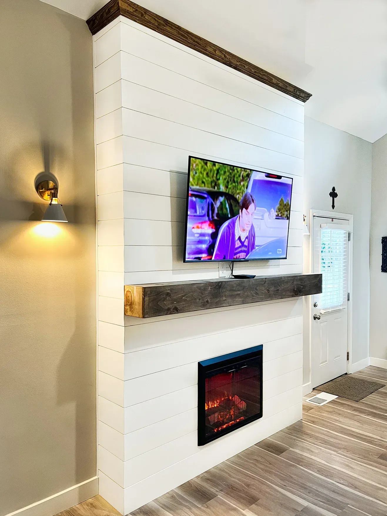 White shiplap fireplace with built-in TV and dark wooden accents. A modern electric fireplace is below the TV.