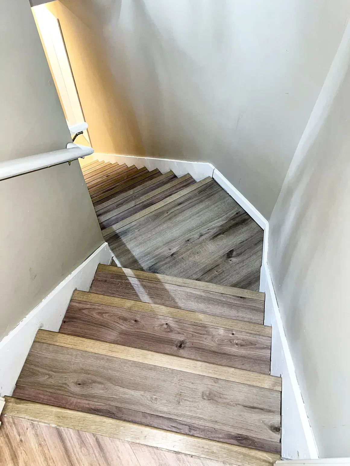 Staircase with wood-look treads, leading down. White trim lines the stairs. Beige walls surround.