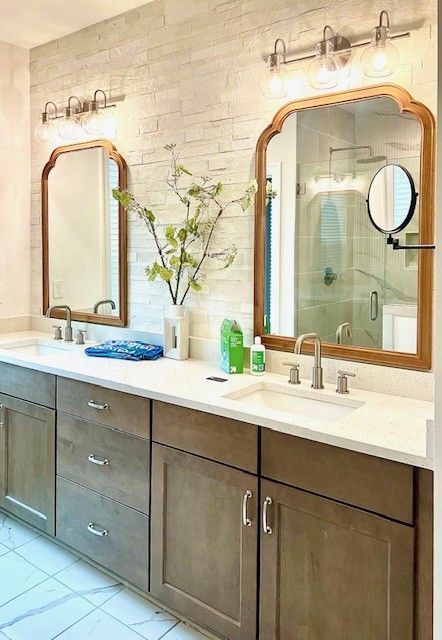 Bathroom with double sinks, two arched mirrors, brick wall, and a neutral color palette.