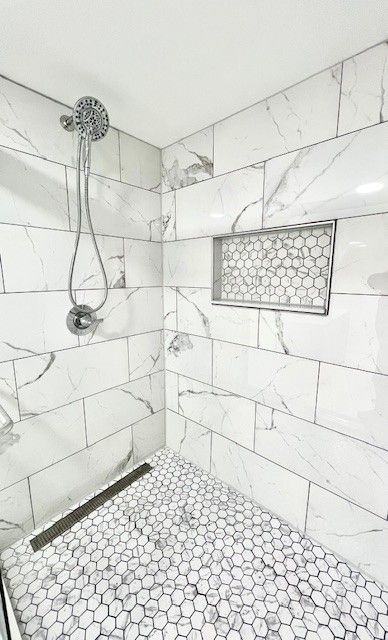 White marble-tiled shower with a niche and hexagon-tiled floor, featuring a linear drain and chrome fixtures.