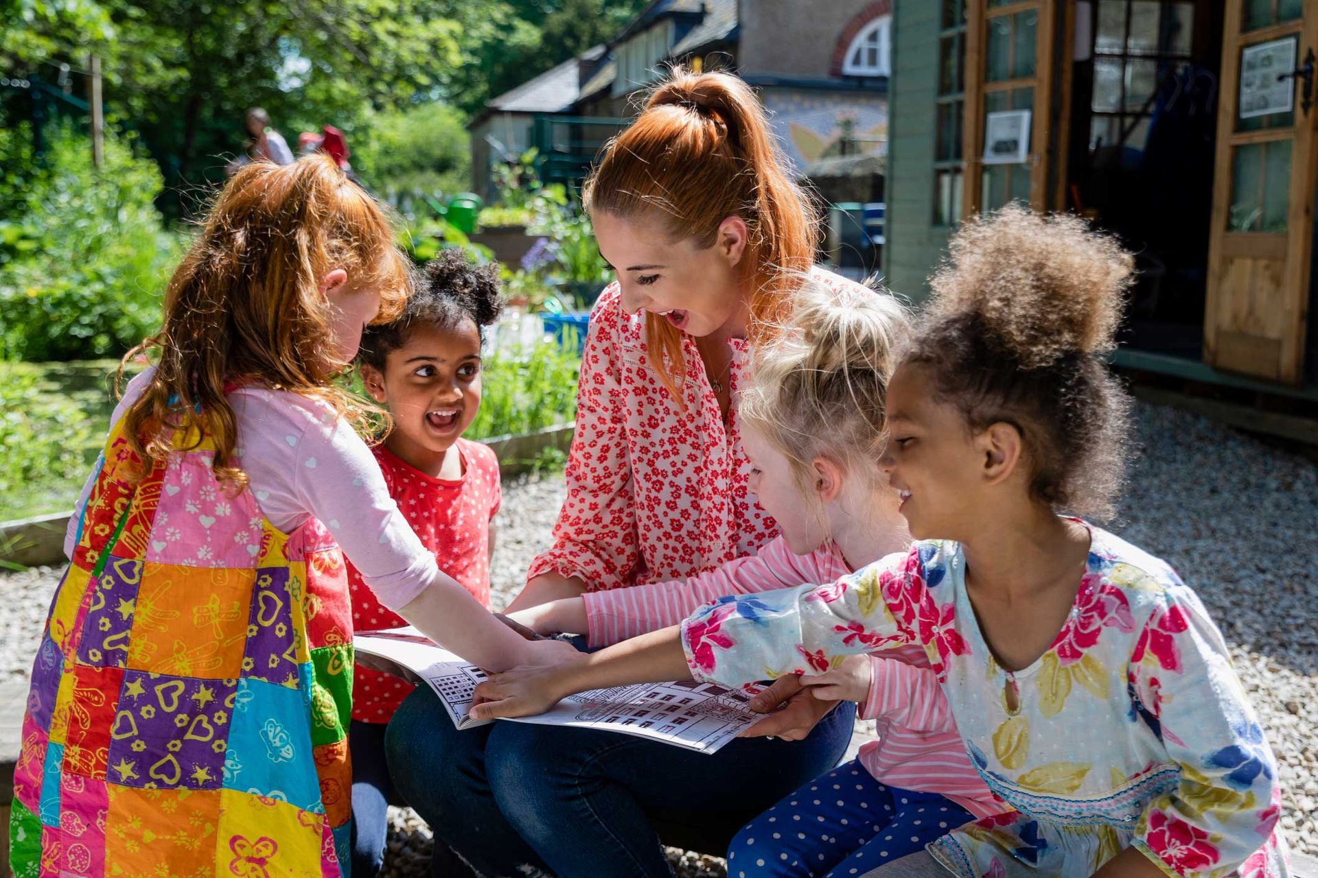Picture of a teacher and her excited little pupils sitting and doing storytime outdoors.