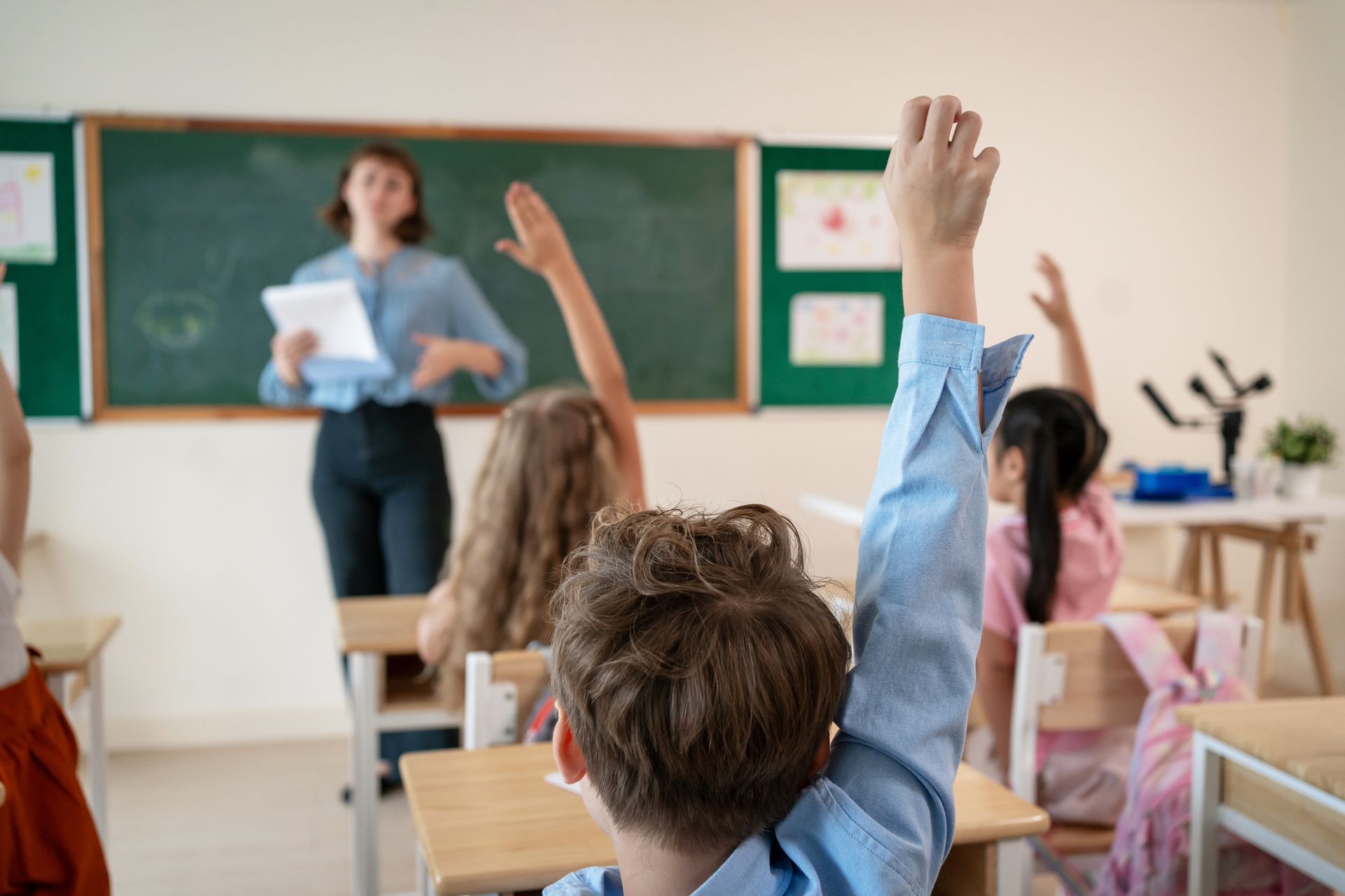 Kids in a classroom raising their hands and actively participating, showcasing child education.