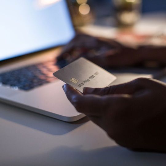 A person is holding a credit card in front of a laptop computer.