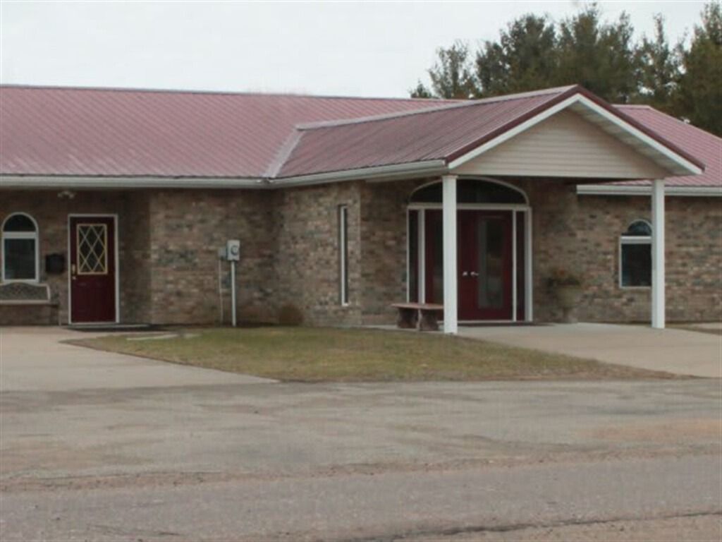 Brick building with red roof; arched doorway with glass doors and a red door.