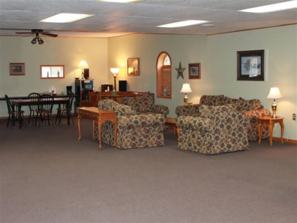 Lounge area with seating, tables, lamps, and a dining table. Light green walls, brown carpet.