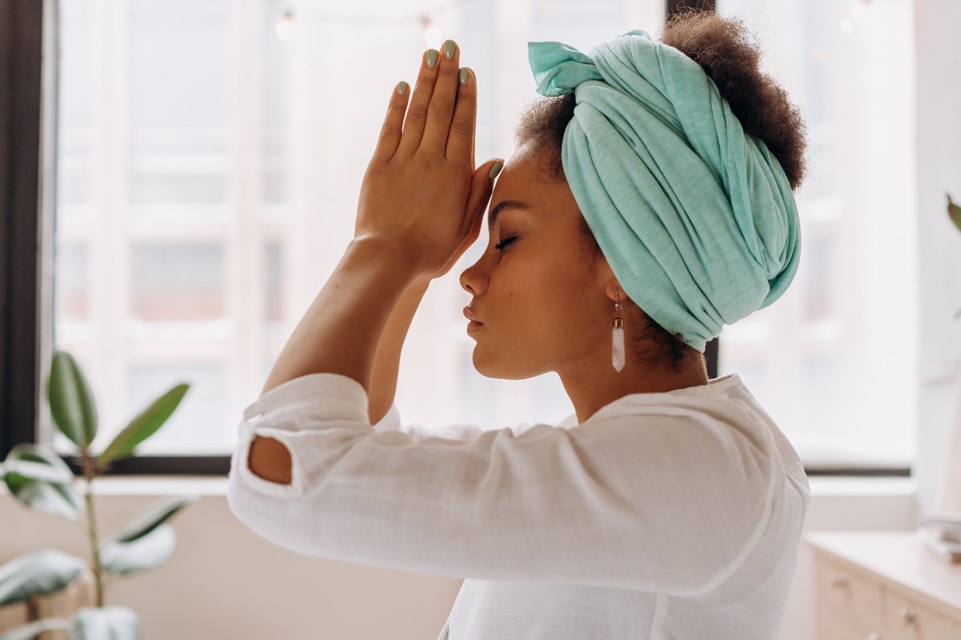 A woman wearing a turban is meditating in front of a window.